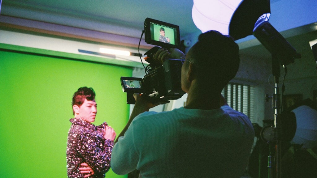 a man films another man on a green set using a Blackmagic Design camera