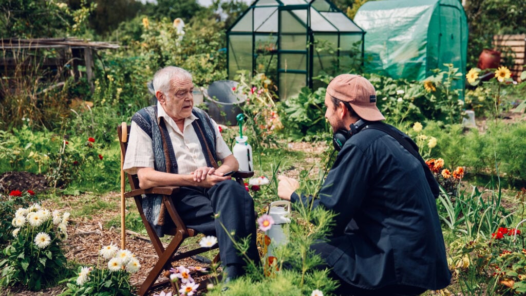 The director talks to an actor on set in a garden setting