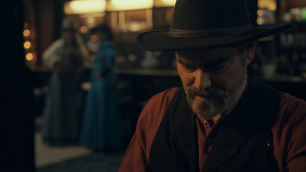 a man in the old west poses for a photo with women in long dresses in the background