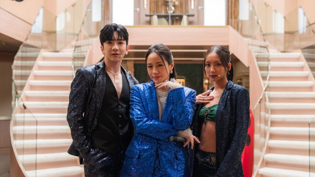 one man and two women wearing stylish sparkly jackets pose in front of a double staircase