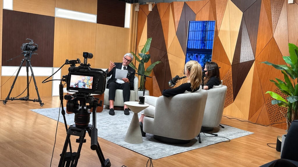 a man and a woman sit on the set of The Vertical Buzz podcast while a Blackmagic 6K Pro Camera films the interview