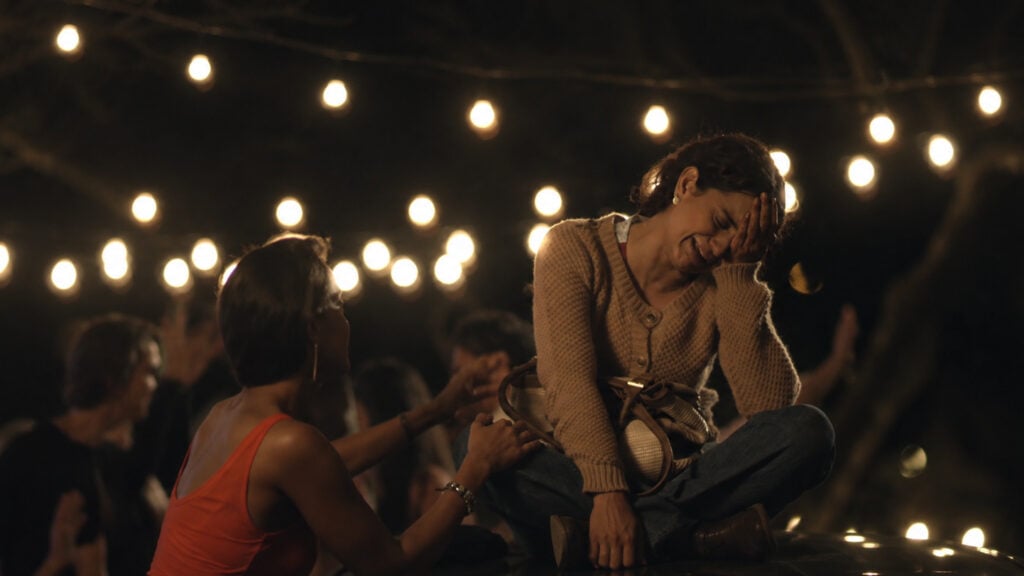 a woman holds her head crying while another woman tries to comfort her