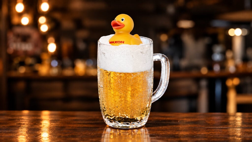 A yellow rubber ducky bearing the name Maxon floats in a mug of beer
