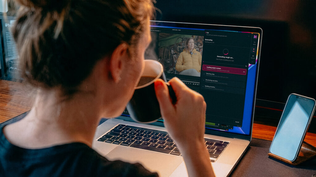 a woman sips a cup of coffee while staring at her computer where she is editing footage on an NLE